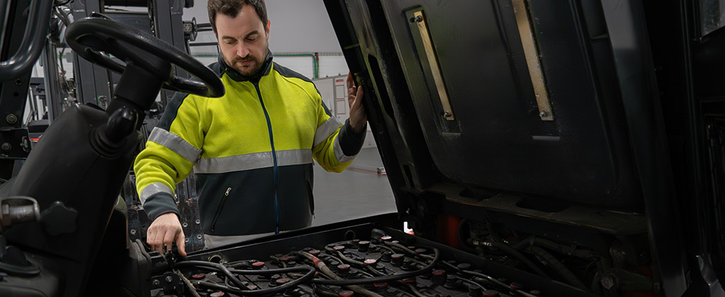 Equipment technician performing maintenance on the battery of a forklift